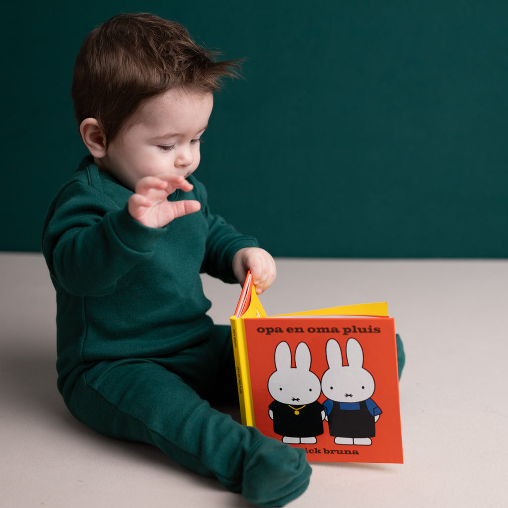 A baby wearing full-bottomed organic cotton trousers, reaching for a Nijntje book 
